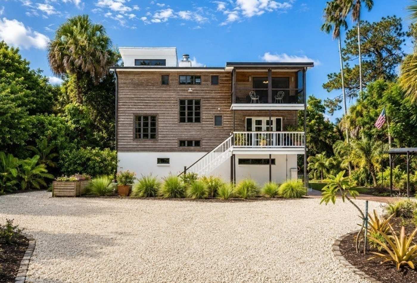 Full exterior of the three-level riverfront home from its landscaped approach