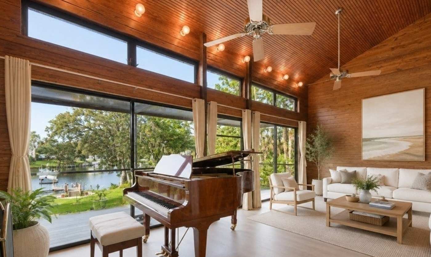 Wood-lined living room with grand piano and windows overlooking the river