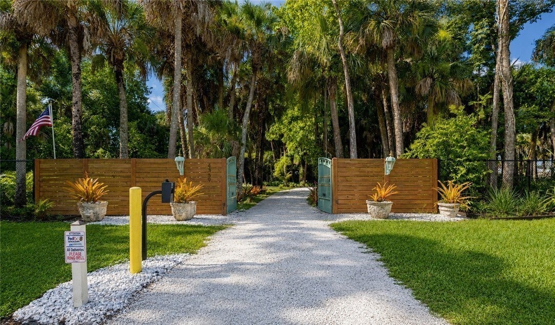 Gated gravel approach lined with palms and greenery