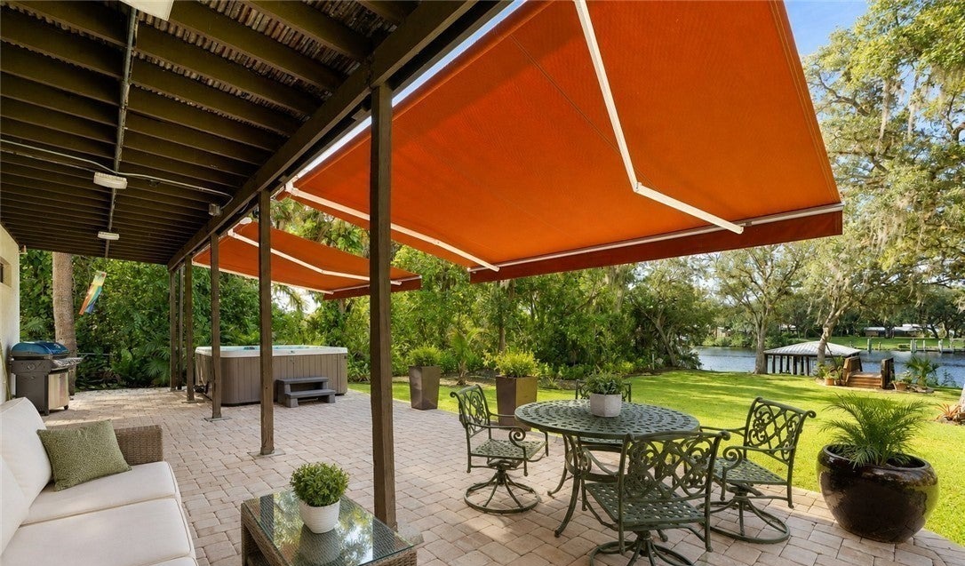 Covered patio with seating and a dining table overlooking the riverfront lawn