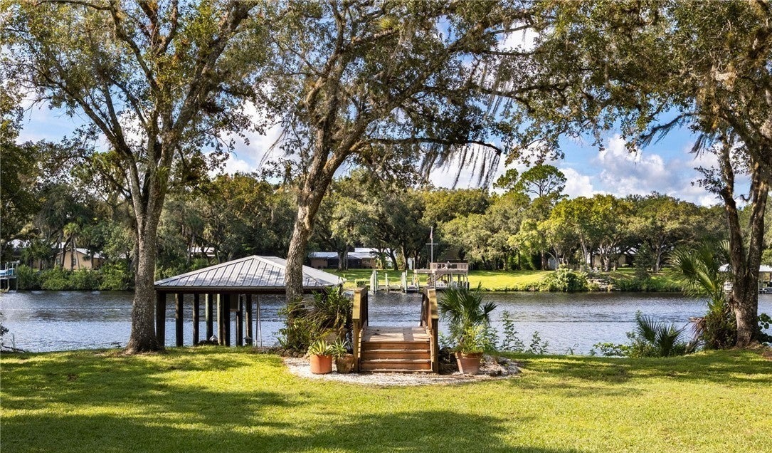 Open lawn beneath trees beside the river, with dock and boathouse